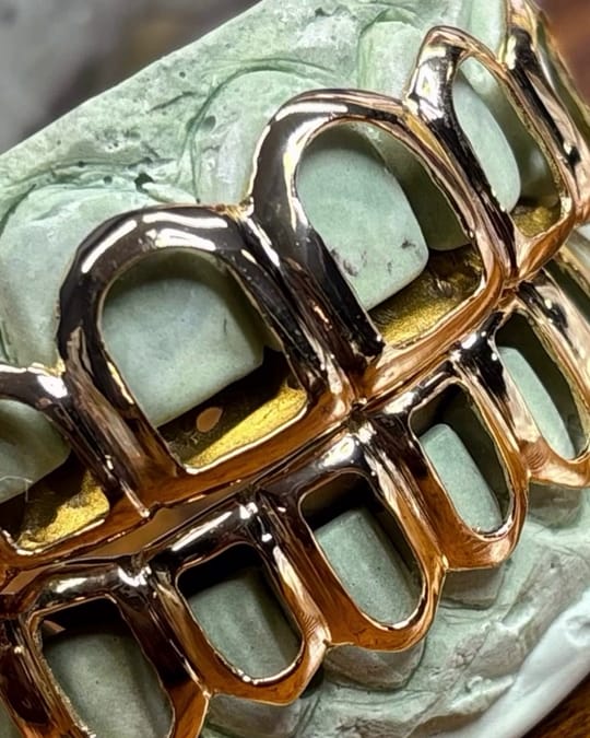 Polished yellow gold open face grillz on a green dental mold